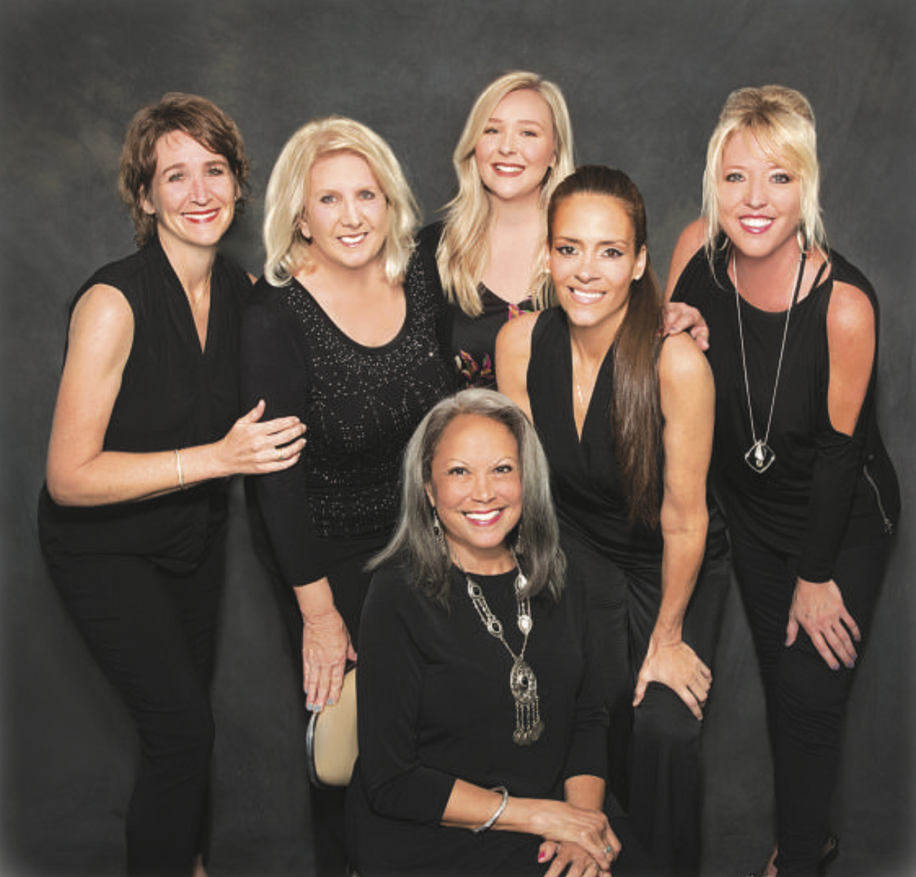 Six women smiling against dark background